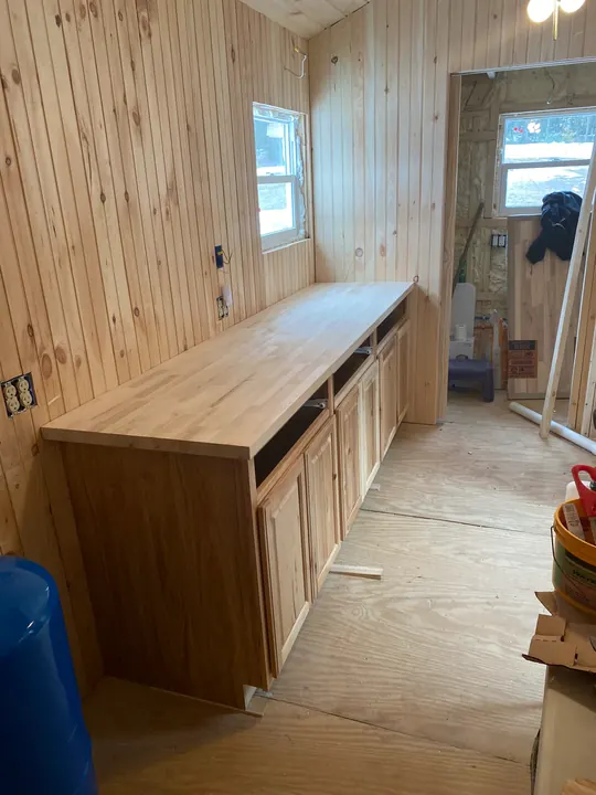 A long run of base cabinets with a wood top along a pine wall
