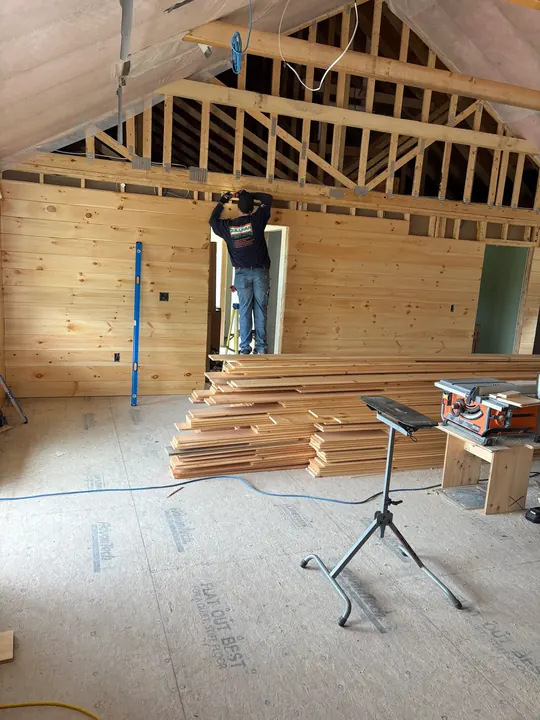 Pine boards going up a tall wall with lumber stacked on the floor