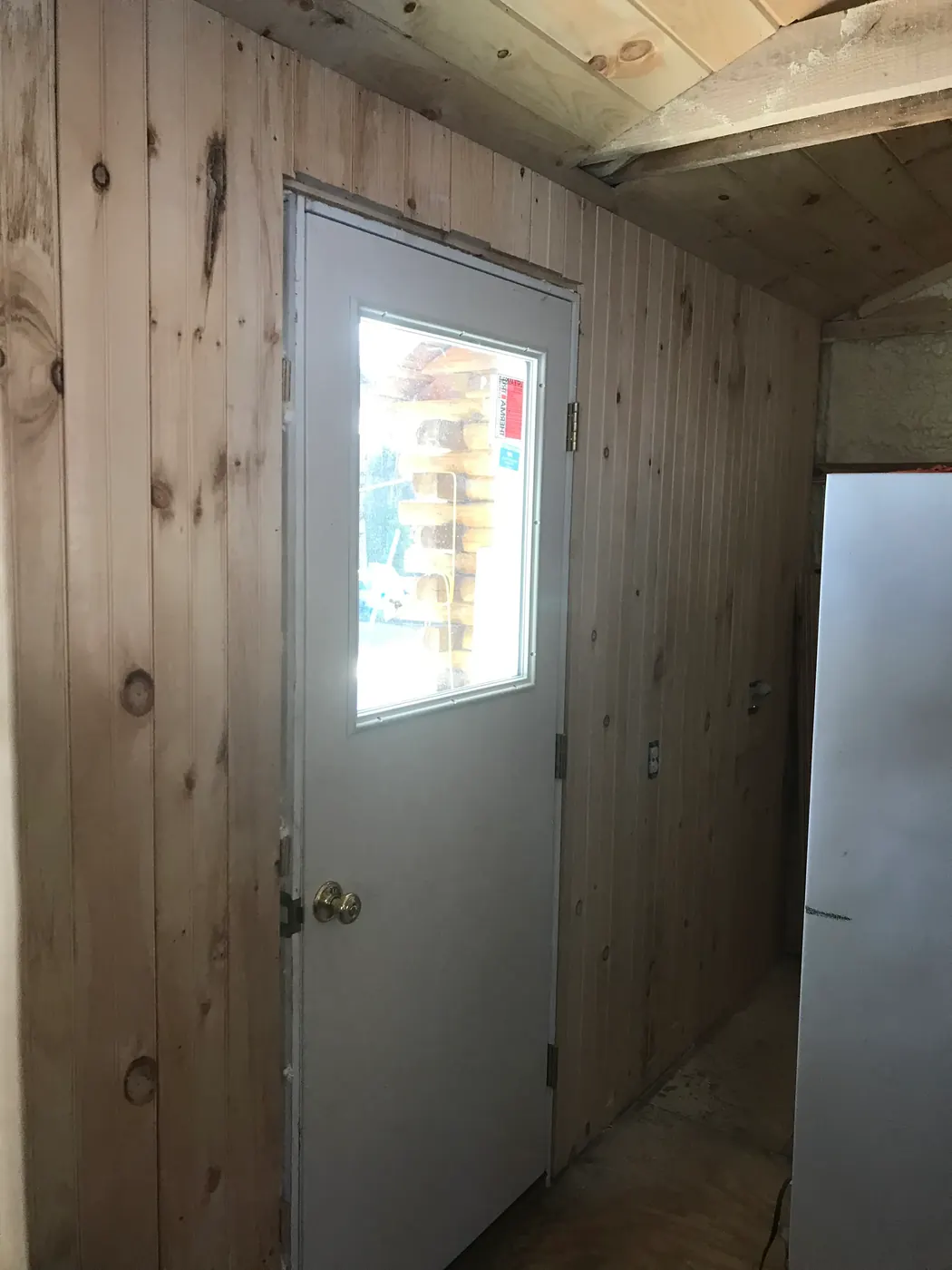 New half-glass door hung and trimmed in a pine-paneled hallway