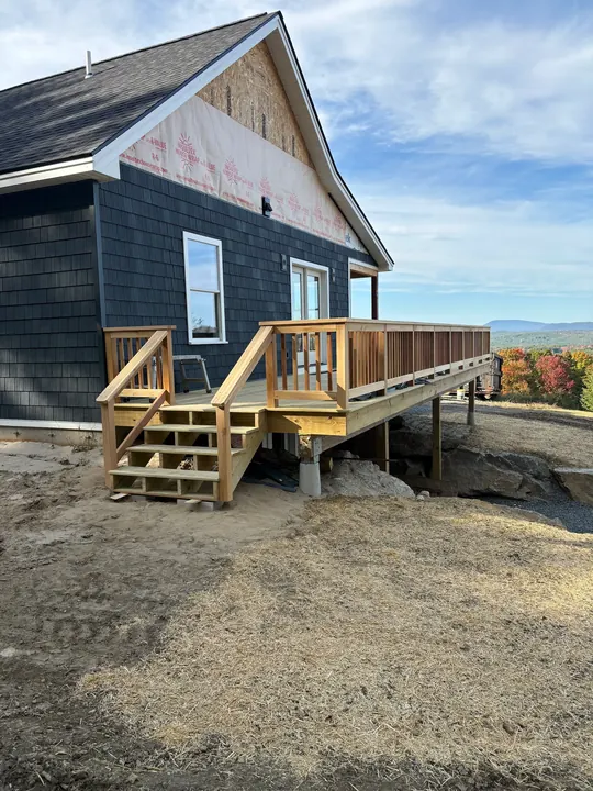 Finished raised deck with stairs and railings beside a house with dark siding