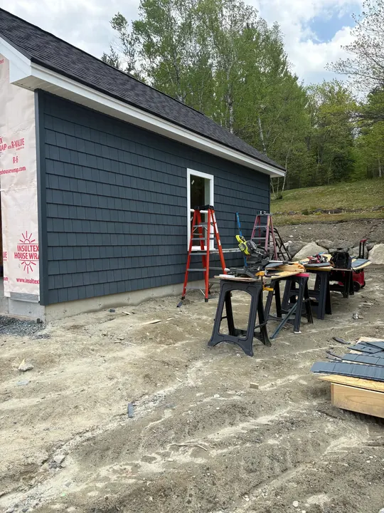 Dark shingle-style siding going up on a new house, gable still in house wrap